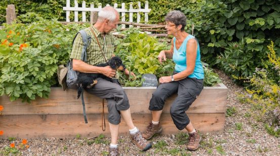 Frau und Mann mit Dackel sitzen an einem Kräutergarten