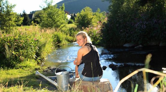 Frau sitzt am Wasser in Olsberg mit Giesskanne